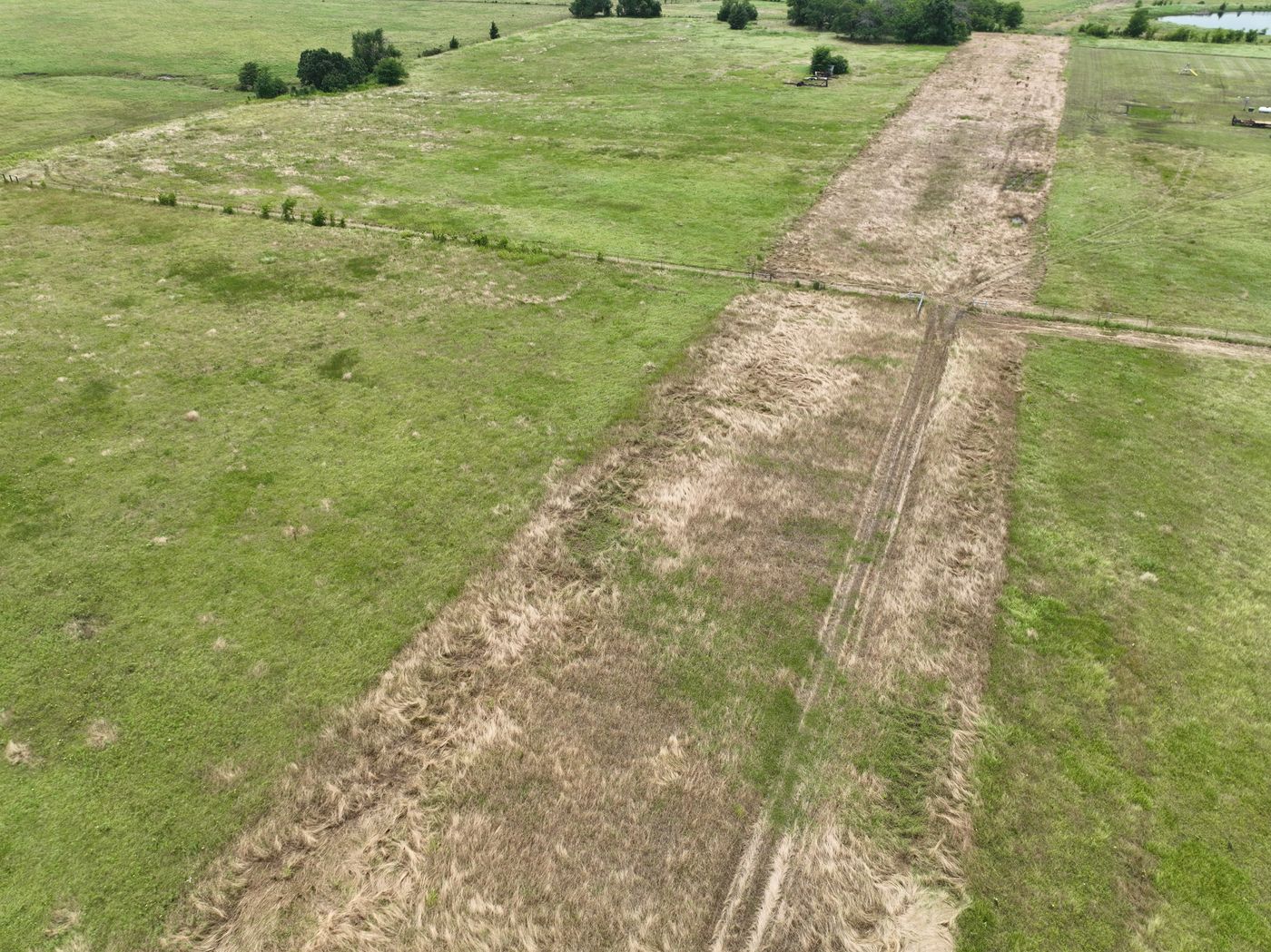 Aerial of a brown dead-grass pipeline corridor through green pasture