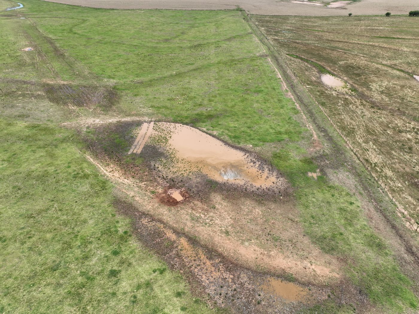 Aerial of ponded water and bare soil along a pipeline right-of-way next to a fence line